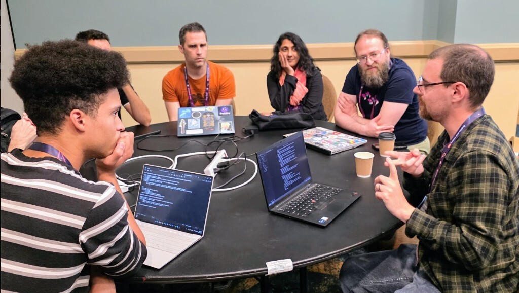 Attendees gather around a round table during the pyOpenSci generative AI open space at PyCon US 2026, laptops open as one participant gestures while leading a small-group discussion.