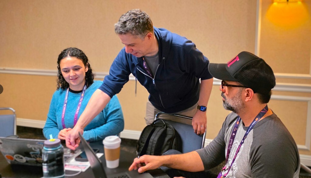 At the pyOpenSci translation table during PyCon US 2026 in Long Beach, Felipe Moreno leans over a laptop to help sprinters add Portuguese translations to the packaging guide while other volunteers work at the same round table.